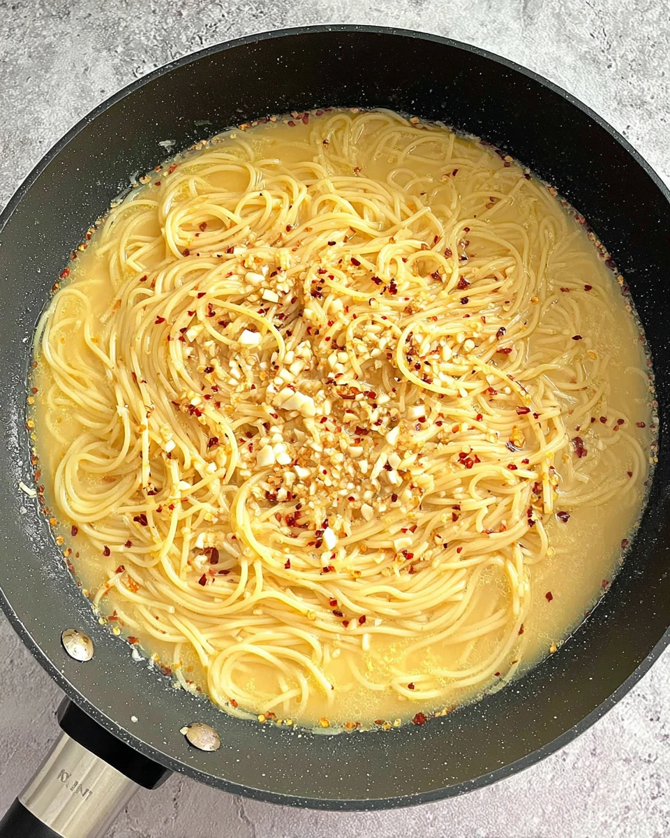 Lemon butter pasta cooking in broth with garlic and red pepper flakes.