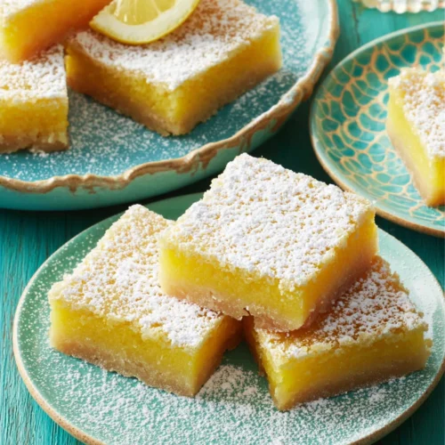 Delicious lemon bars dusted with powdered sugar on plates.