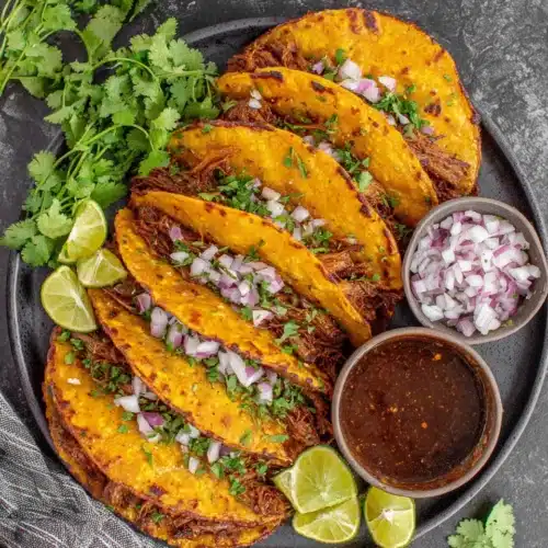 Delicious crock pot birria tacos served with garnishes.