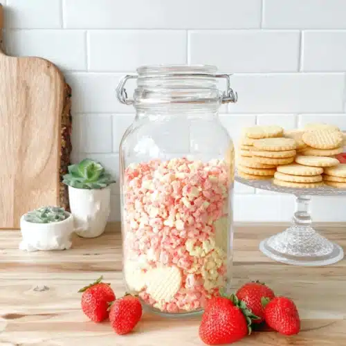Strawberry crunch bars in a glass jar with fresh strawberries and cookies nearby