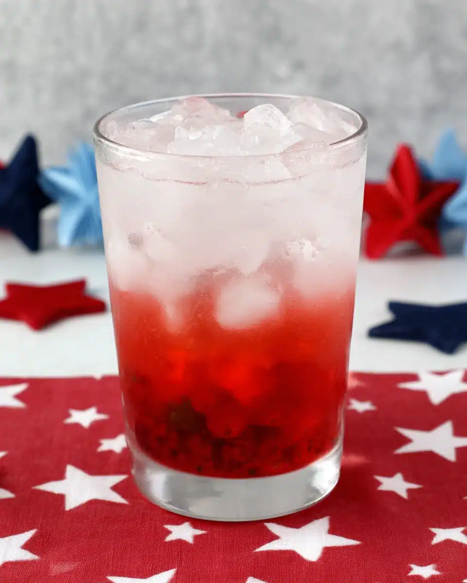 4th of July Mojito with Red Berry Layer and Stars 4th of July Mojito with red berry layer and ice in a clear glass on a star-patterned red cloth.