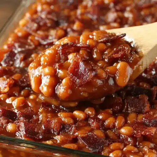 Hearty baked beans with bacon in a glass dish, served with a wooden spoon
