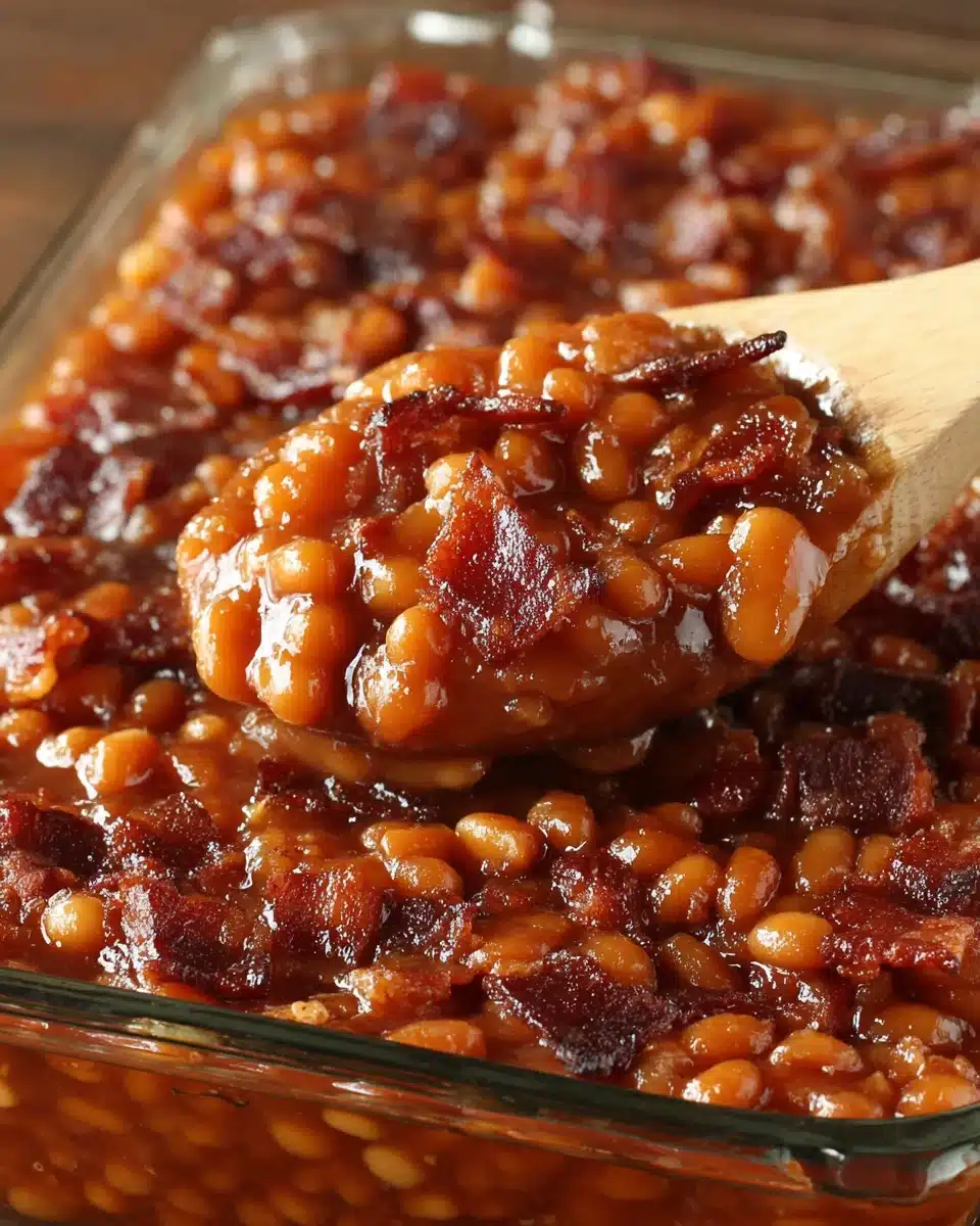 Hearty baked beans with bacon in a glass dish, served with a wooden spoon