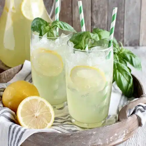 Two glasses of basil lemonade with lemon slices and basil garnish on a tray