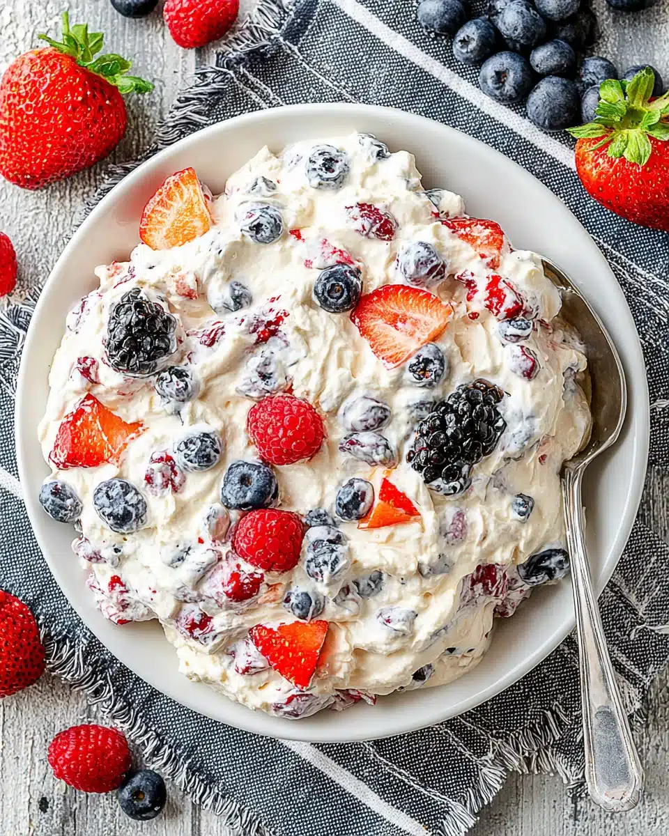 Berry cheesecake salad with fresh strawberries, blueberries, raspberries, and blackberries on a white plate.