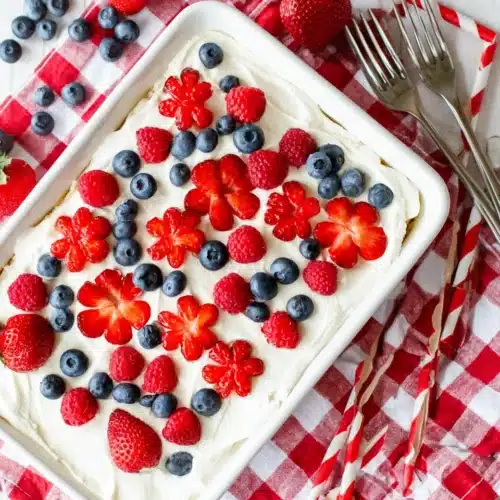 Berry tiramisu topped with fresh strawberries, raspberries, and blueberries on a checkered cloth