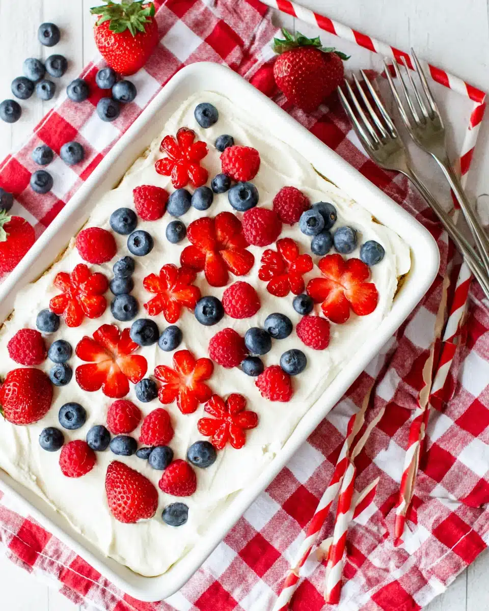 Berry tiramisu topped with fresh strawberries, raspberries, and blueberries on a checkered cloth