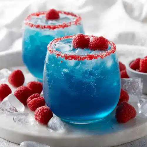 Two glasses of blue Hawaiian lemonade punch with raspberry garnish and ice