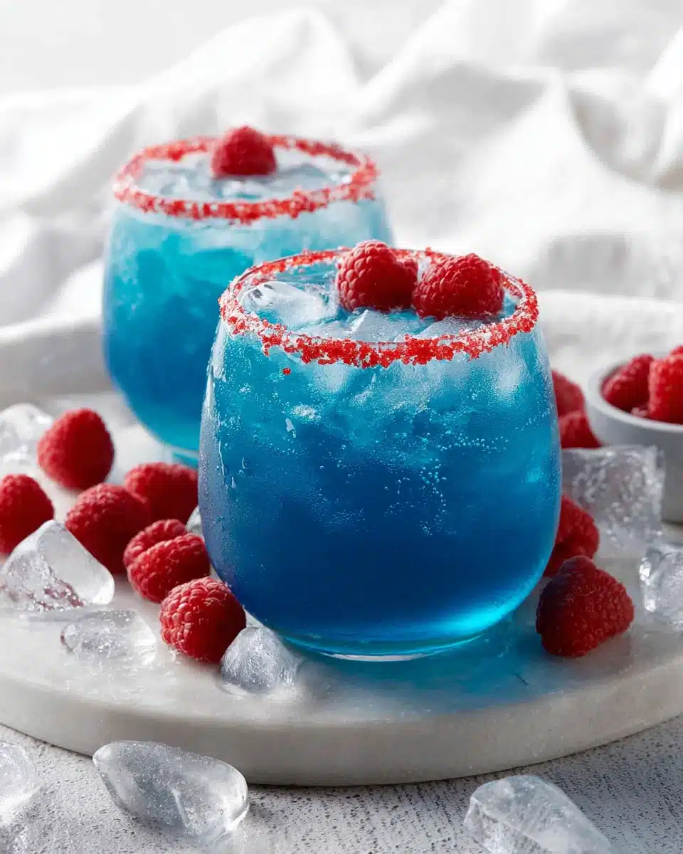 Two glasses of blue Hawaiian lemonade punch with raspberry garnish and ice