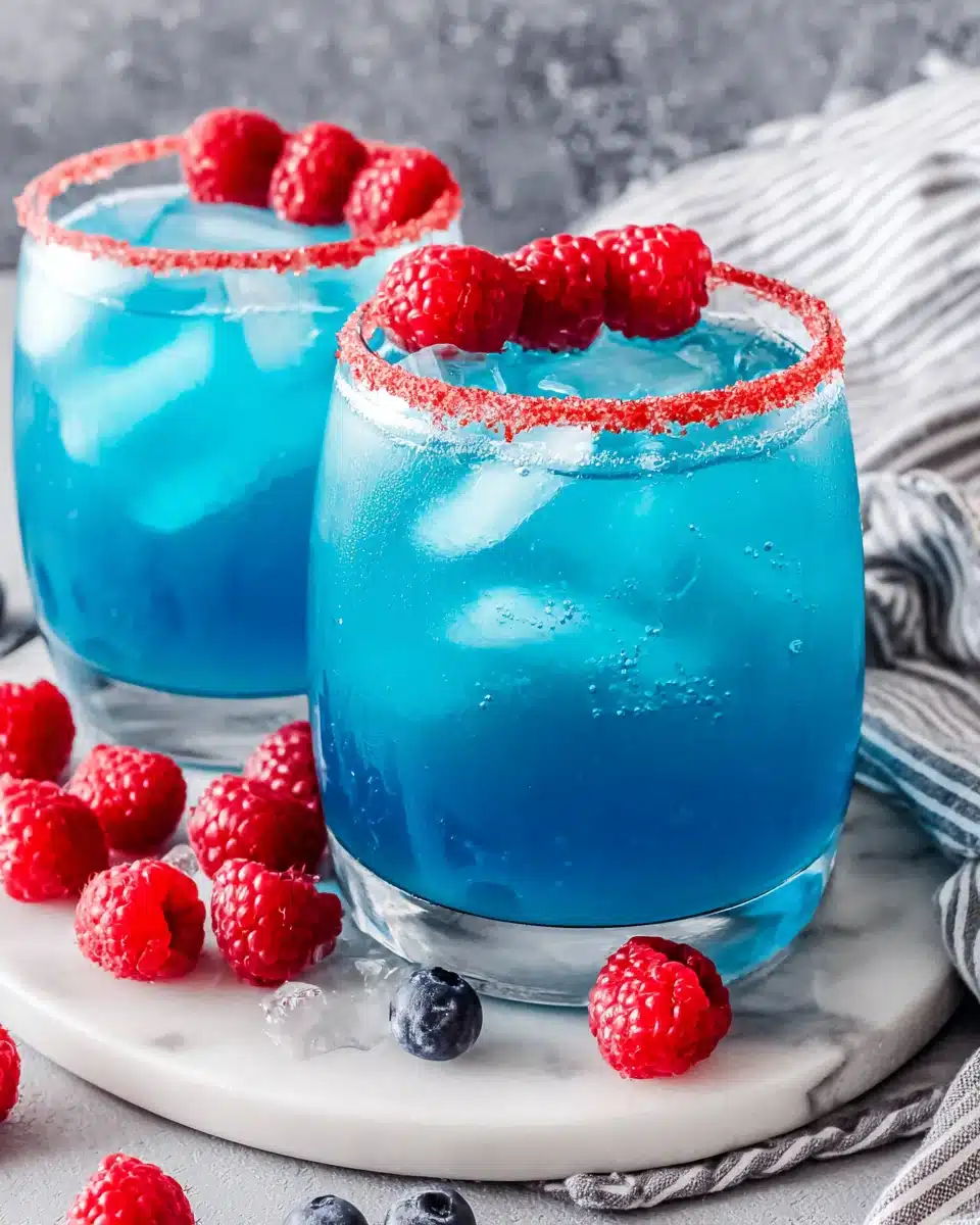 Blue Hawaiian lemonade punch in glasses with ice and raspberry garnish