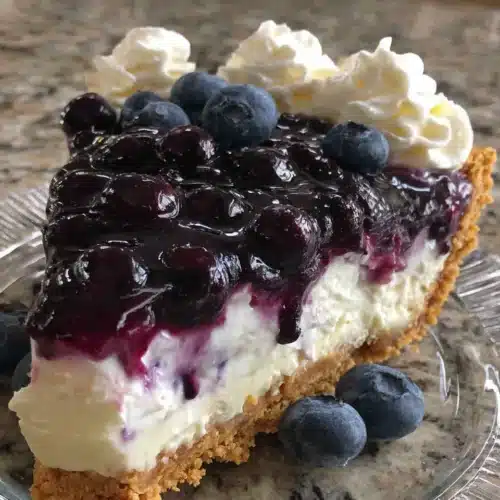 A slice of blueberry cream cheese pie with graham cracker crust and fresh blueberry topping