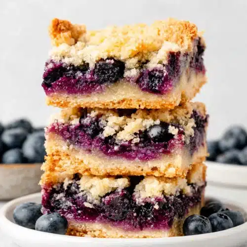 Stack of three blueberry crumble bars with golden topping and juicy berry filling
