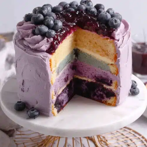 Blueberry layer cake with purple frosting and fresh blueberries, slice cut to show layers