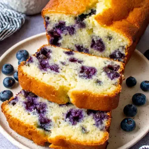 Sliced blueberry muffin bread on a plate with fresh blueberries