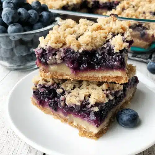 Blueberry oat crumble bars stacked on a white plate with fresh blueberries nearby.
