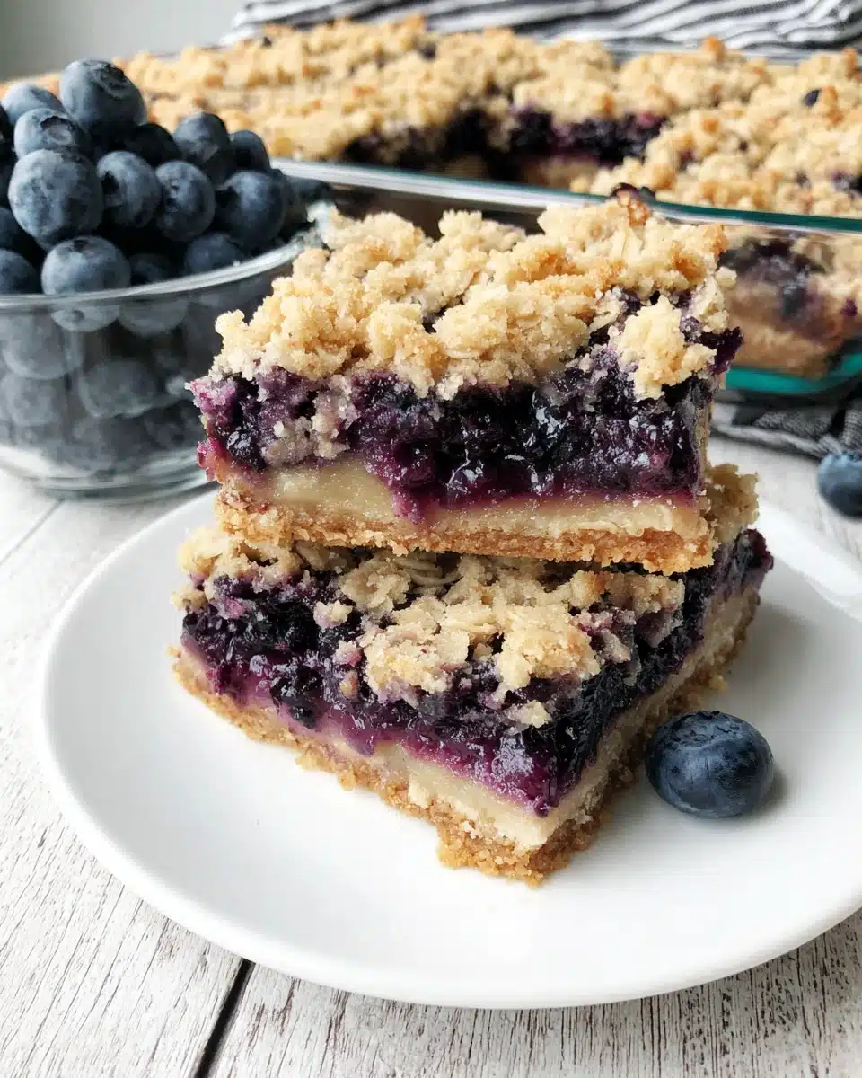 Blueberry oat crumble bars stacked on a white plate with fresh blueberries nearby.