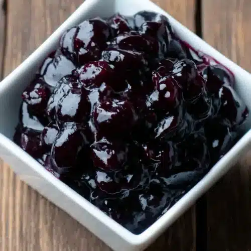 Glossy blueberry sauce in a white bowl on a wooden surface