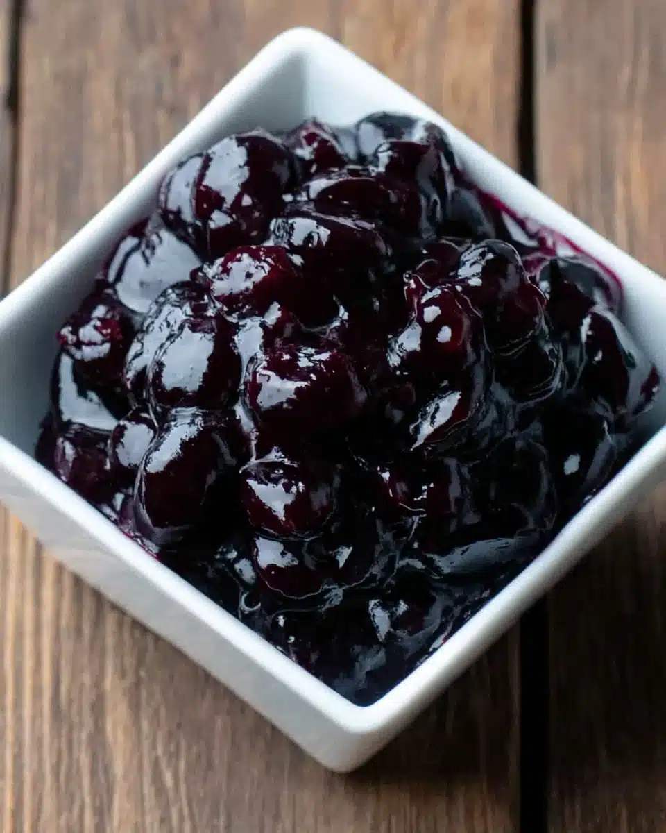 Glossy blueberry sauce in a white bowl on a wooden surface