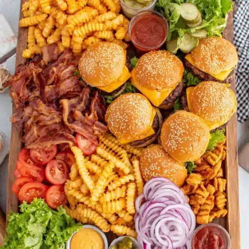Burger board with patties, buns, toppings, condiments, and fries arranged on a wooden tray