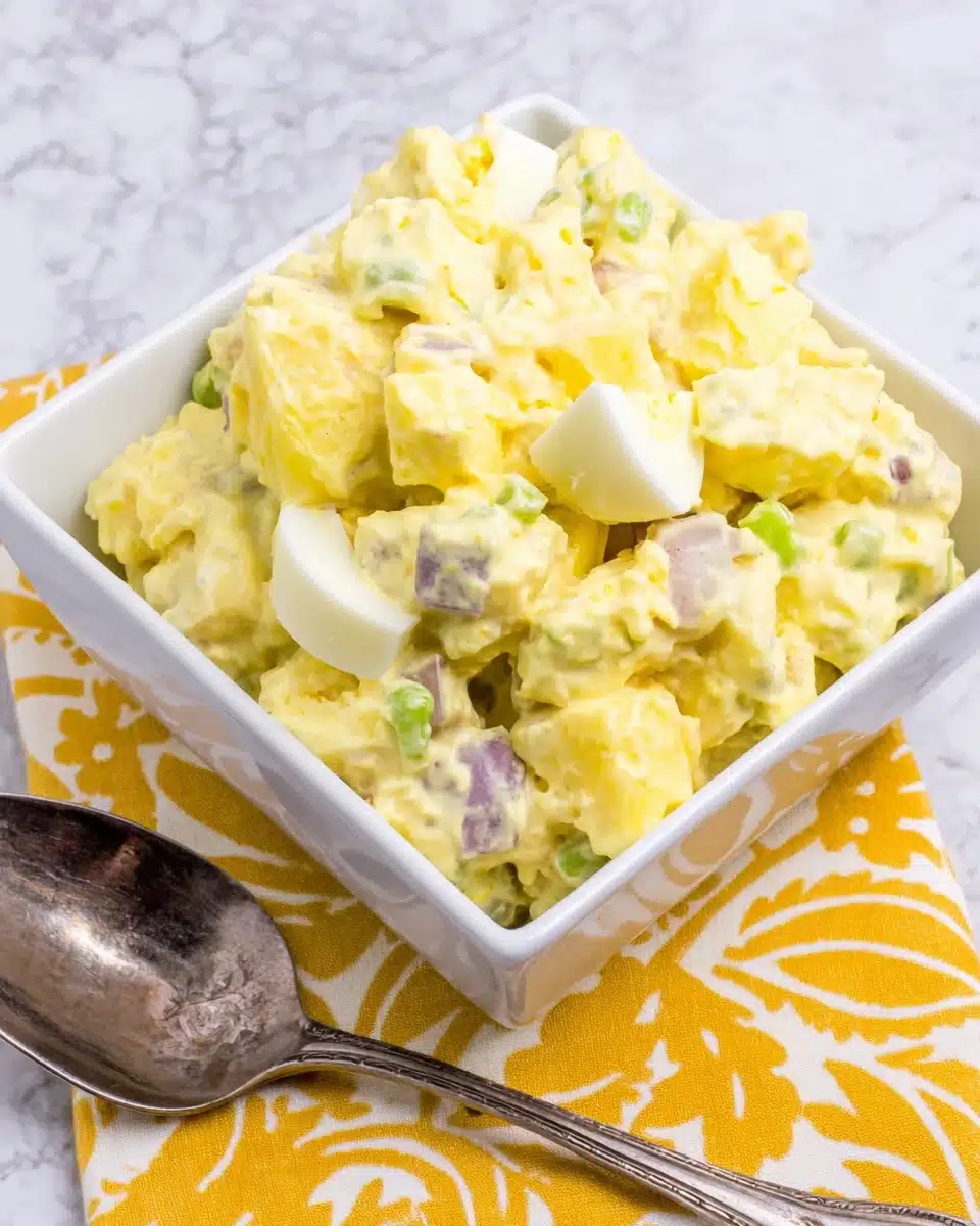 Classic potato salad in a white bowl with a spoon, served on a yellow napkin