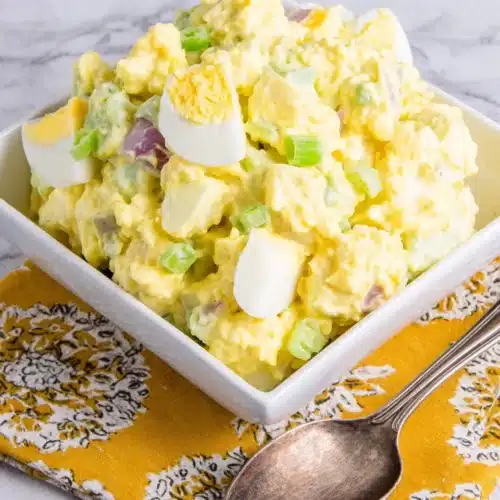 Classic potato salad in a white bowl with a spoon, served on a yellow napkin