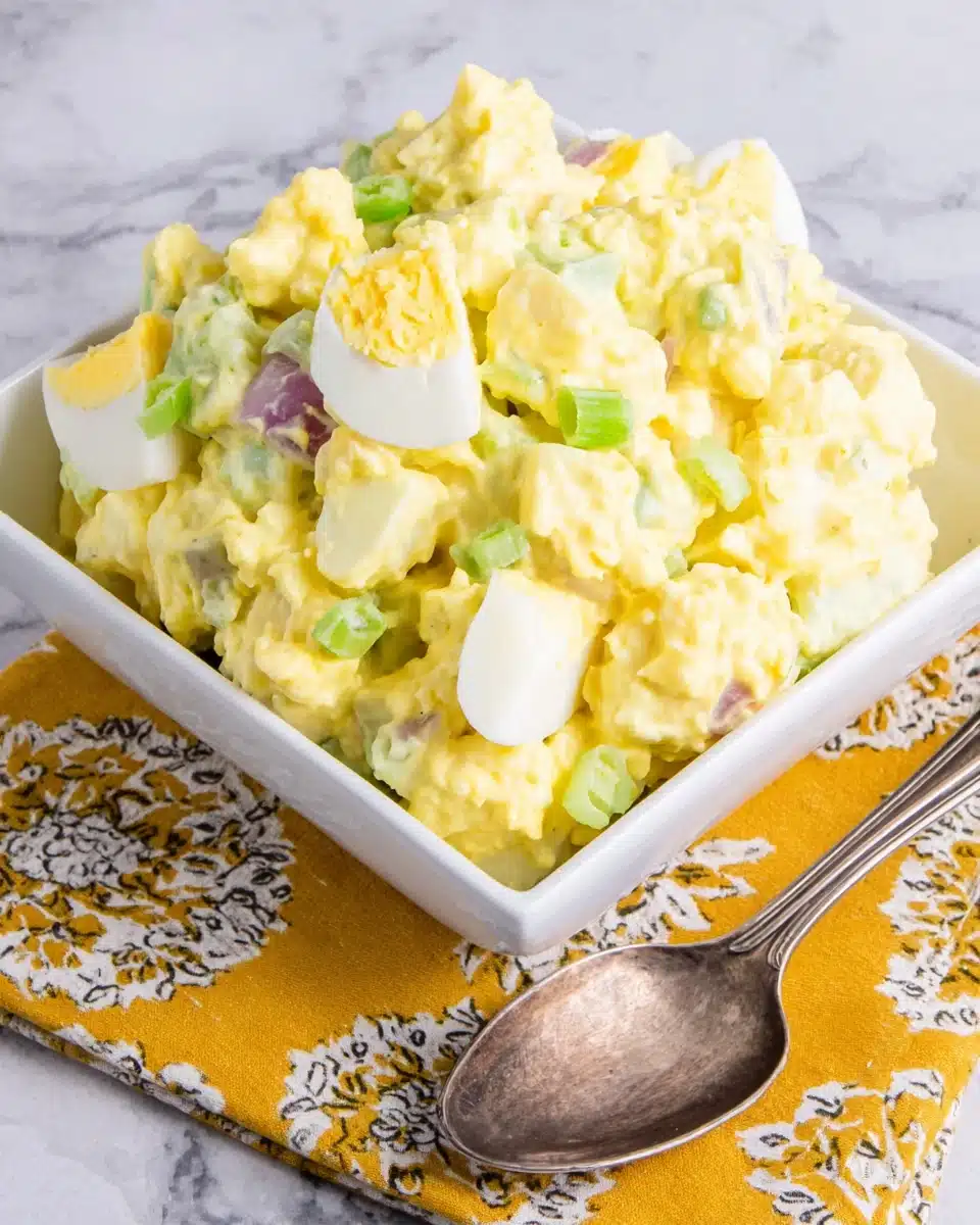 Classic potato salad in a white bowl with a spoon, served on a yellow napkin