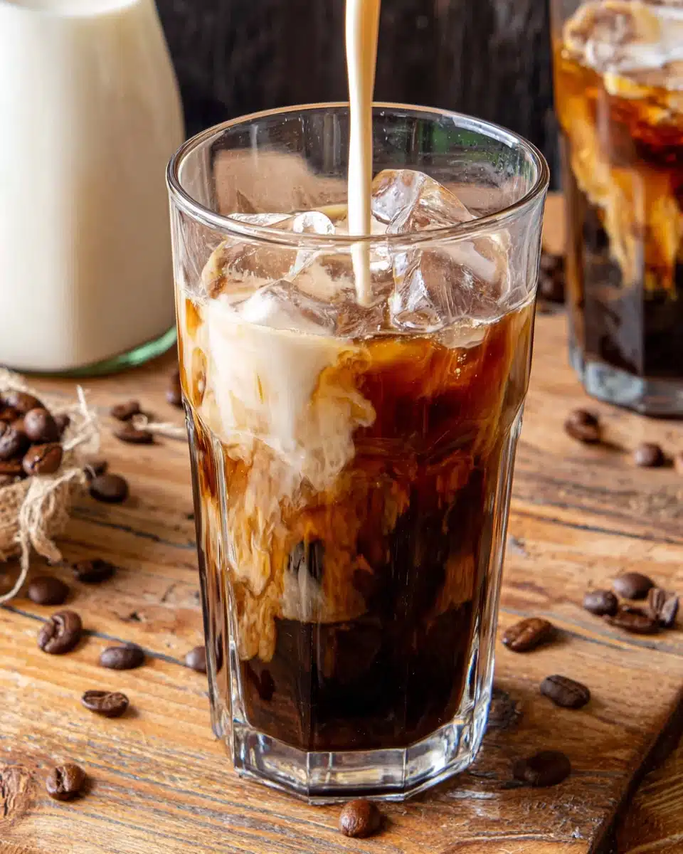 Cold brew coffee with cream and ice in a glass, surrounded by coffee beans