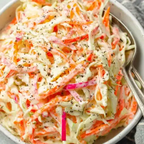 Creamy cole slaw salad with cabbage, carrots, and apple in a white bowl