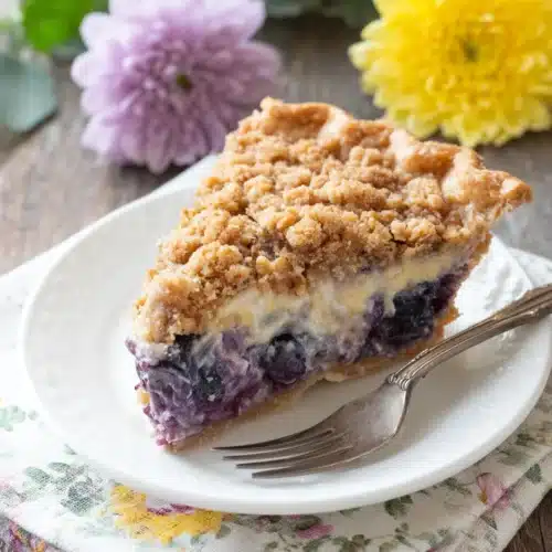 A slice of creamy blueberry pie with crumb topping on a white plate