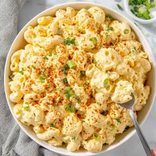 Creamy deviled egg macaroni salad in a white bowl with green onions and paprika