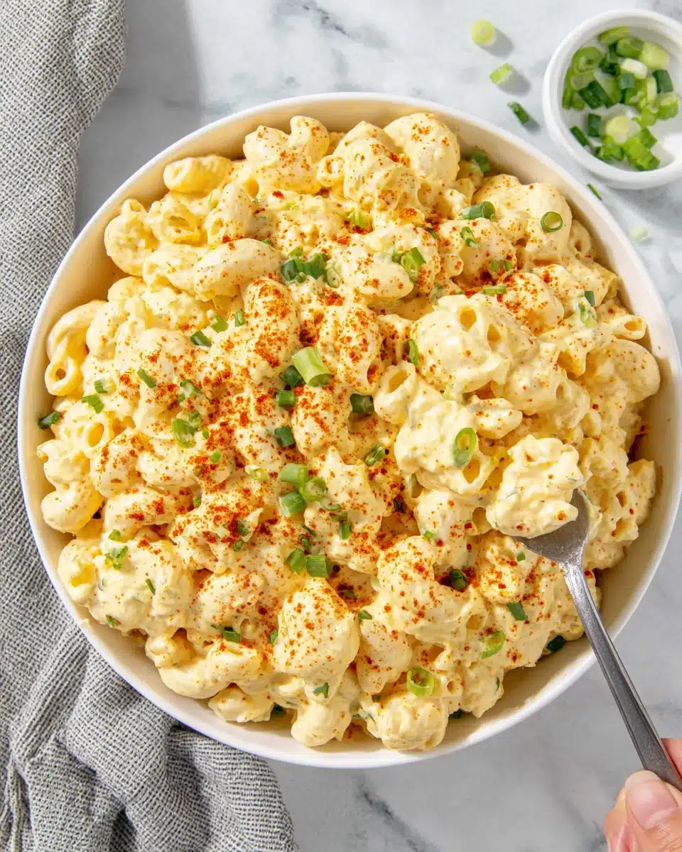 Creamy deviled egg macaroni salad in a white bowl with green onions and paprika