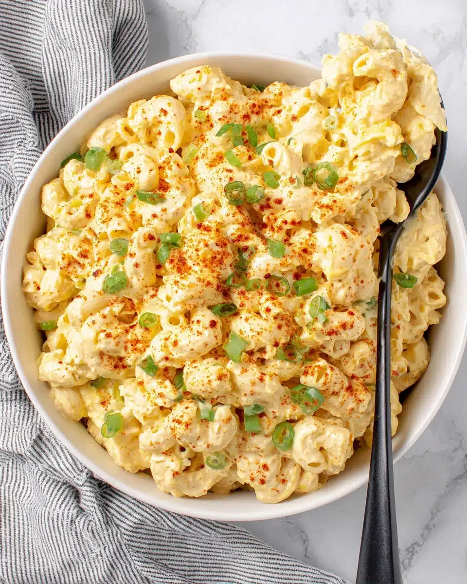 Creamy deviled egg macaroni salad in a white bowl with green onions and paprika