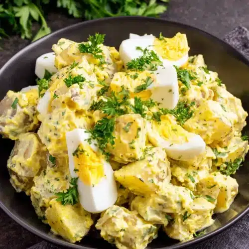 Creamy deviled egg potato salad in a black bowl, garnished with parsley