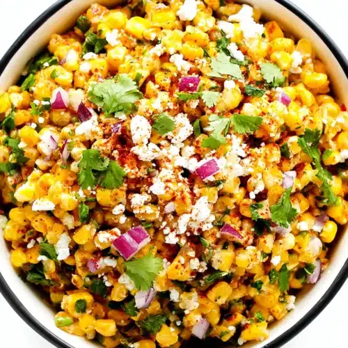Easy elote dip in a white bowl with black rim, topped with cheese, cilantro, and chili powder.