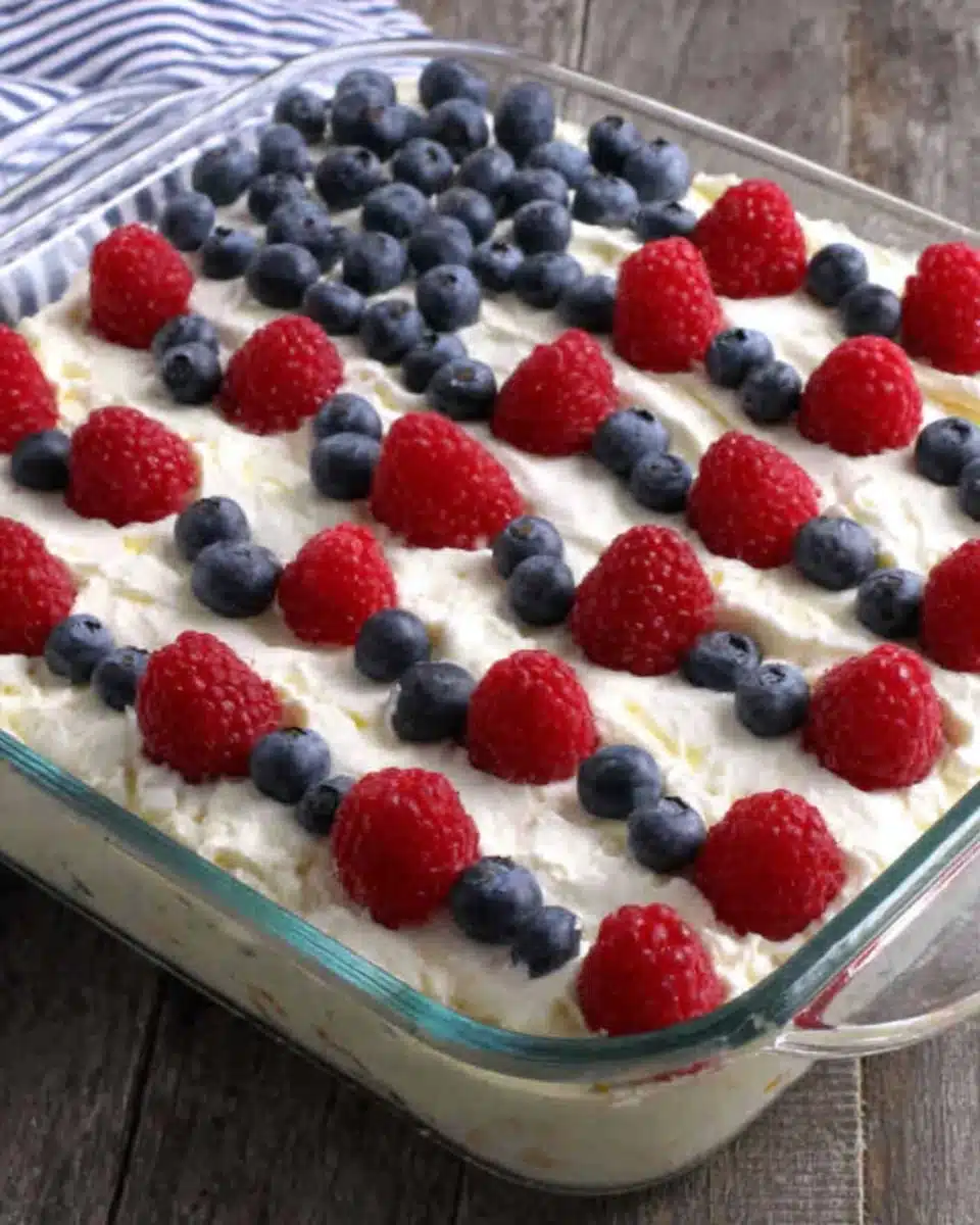 Easy flag cake with red raspberries and blueberries arranged in an American flag design on white whipped topping