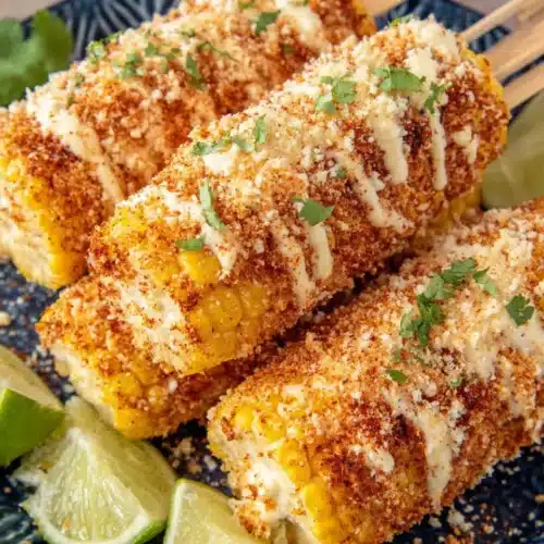 Creamy elote recipe with cotija cheese, chili powder, and lime on corn cobs