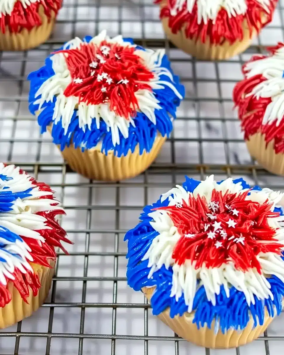 Colorful firework cupcakes with red, white, and blue frosting and silver stars on a cooling rack