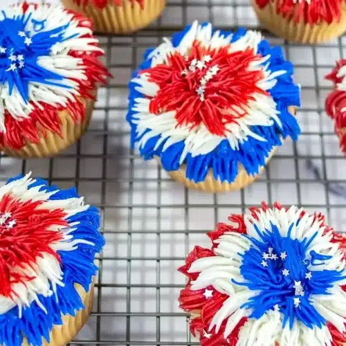 Colorful firework cupcakes with red, white, and blue frosting and silver stars on a cooling rack