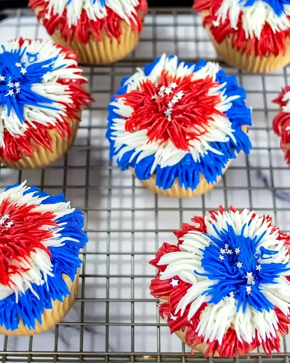 Colorful firework cupcakes with red, white, and blue frosting and silver stars on a cooling rack