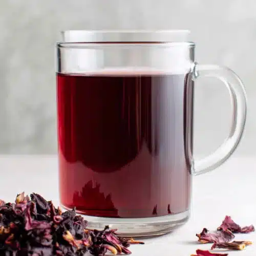 A glass mug of hibiscus tea with dried petals nearby