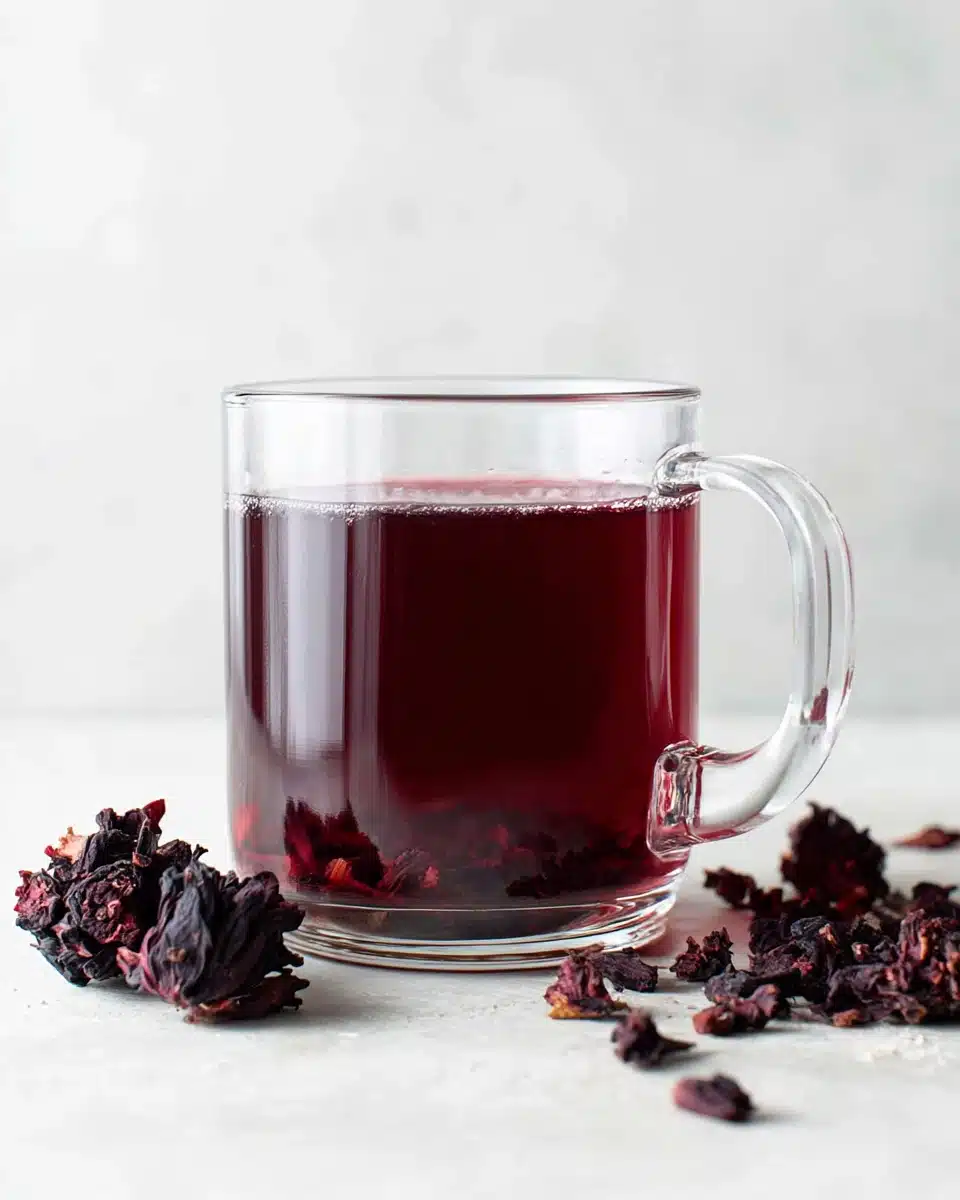 Glass mug of hibiscus tea with dried hibiscus flowers nearby