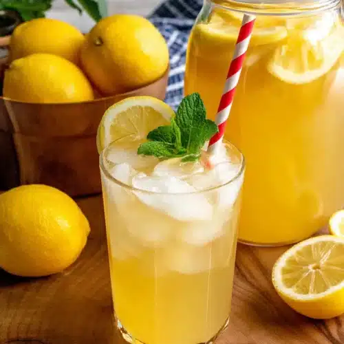 Homemade lemonade in a mason jar with ice, mint, and lemon slice, pitcher in background