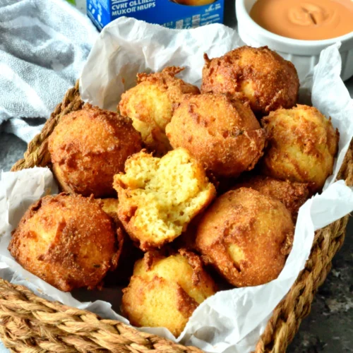 Crispy golden hush puppies in a basket with Jiffy mix and dipping sauce