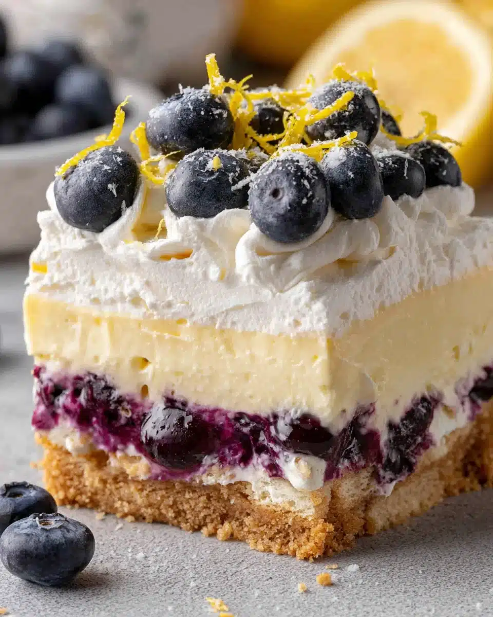 Lemon blueberry lush dessert slice with layers of crust, lemon cream, blueberry filling, and whipped topping.