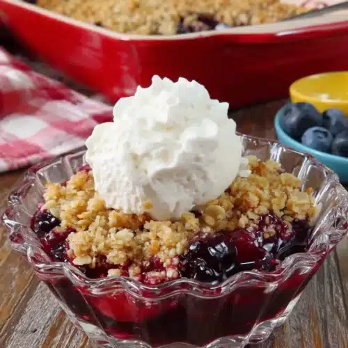 Mini blueberry crisp in a glass dish with whipped cream