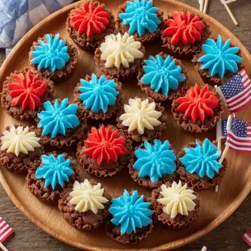 Mini brownie bites with red, white, and blue frosting on a wooden board with American flags