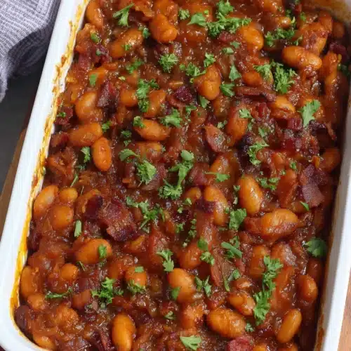 Paula Deen baked beans in a white dish, garnished with parsley