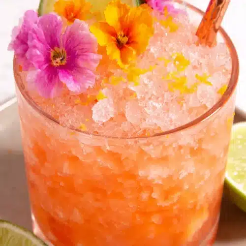 Pineapple mango rum punch in a glass with ice, lime, and edible flowers