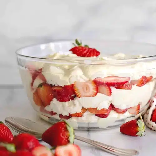 Punch bowl cake with layers of cake, pudding, and strawberries in a glass bowl