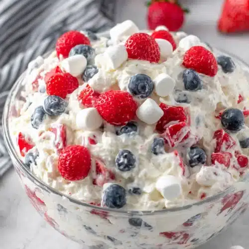Red white and blue cheesecake salad with fresh berries and marshmallows in a glass bowl